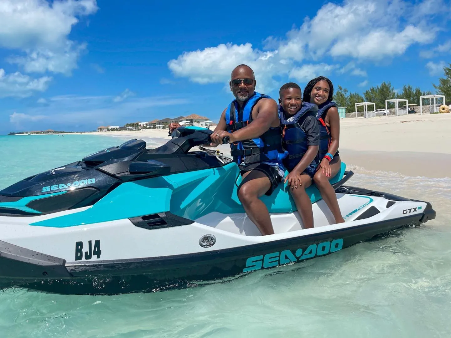 Three riders on a SeaDoo GTX jet ski at the water's edge on a Bimini beach