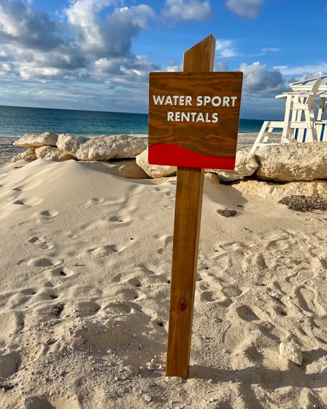 A wooden Water Sport Rentals sign on the sand at a Bimini beach